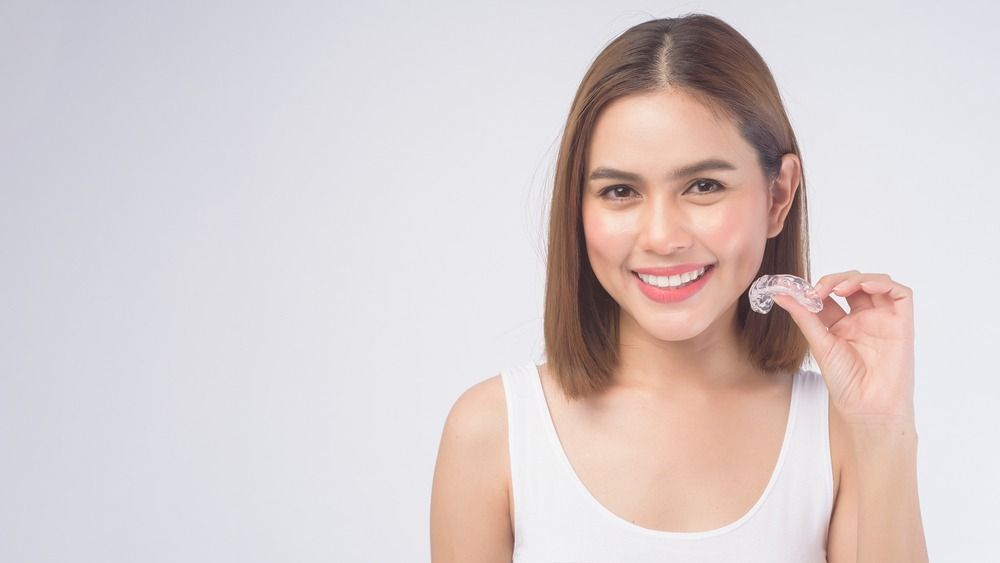 Smiling woman holding a clear dental aligner against a white background