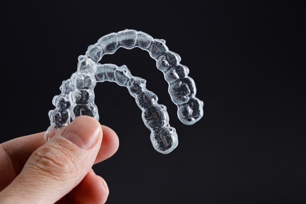 Clear aligner held in hand against a dark background
