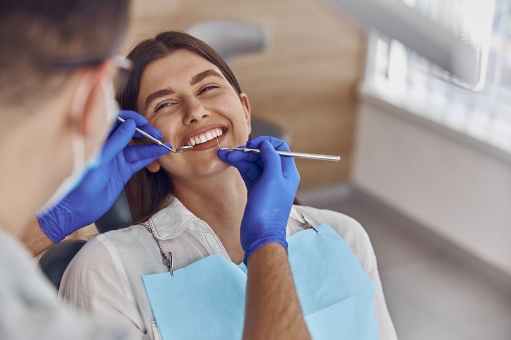 Dentist examining a smiling patient’s teeth with dental tools and blue gloves in a clinic