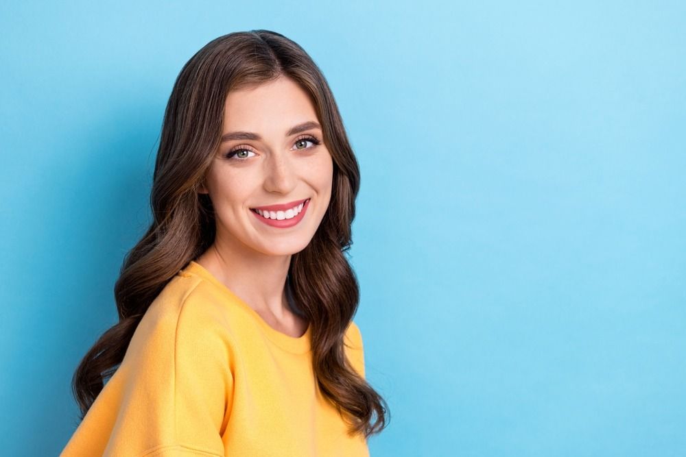 Smiling woman in a yellow top against a blue background