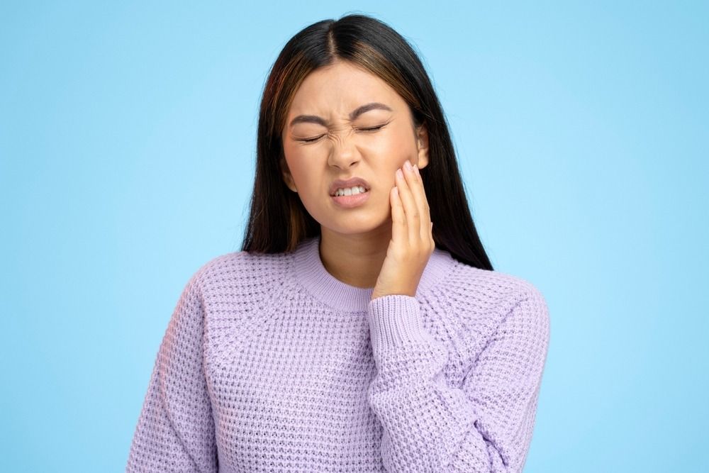 Person in a lavender sweater holding their cheek