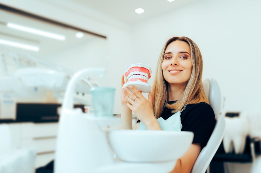 Woman holding a dental model in a bright clinic, smiling beside a sink