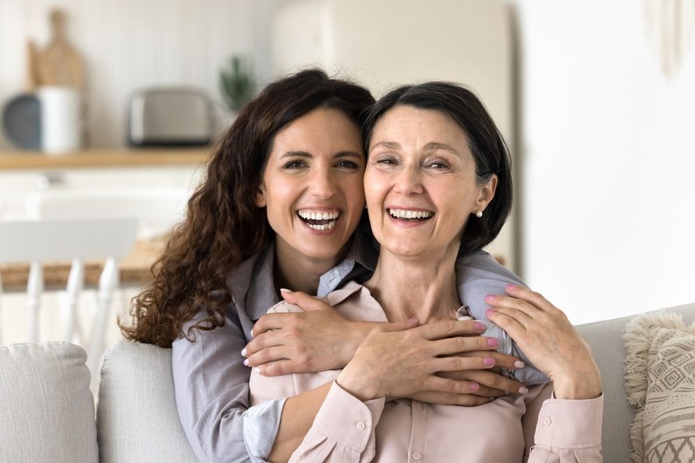 Two smiling women hugging on a couch in a bright living room