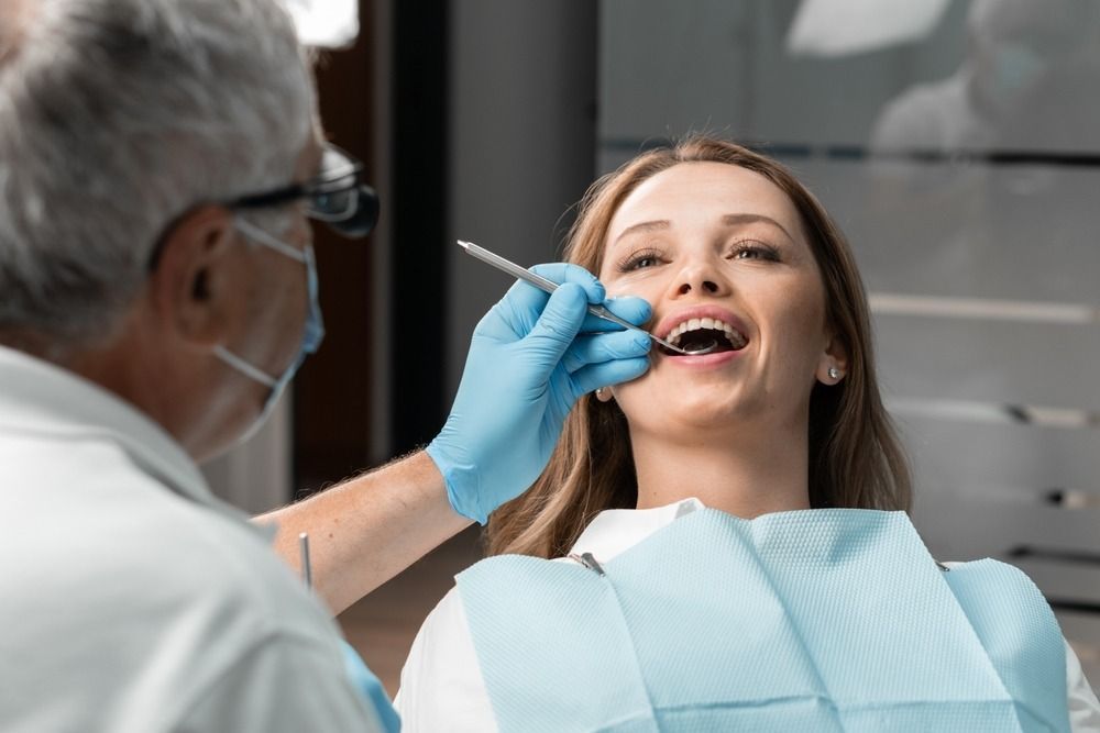Dentist examining a smiling patient in a dental chair with gloved hand and dental tool