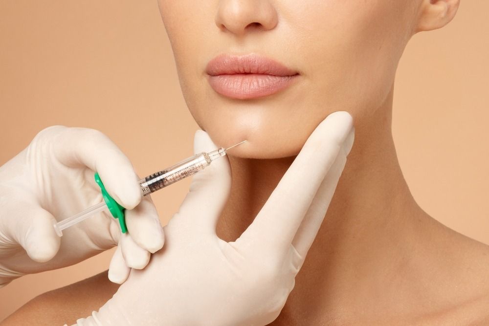 Injector giving lip filler to a woman’s chin in a clinical close-up.