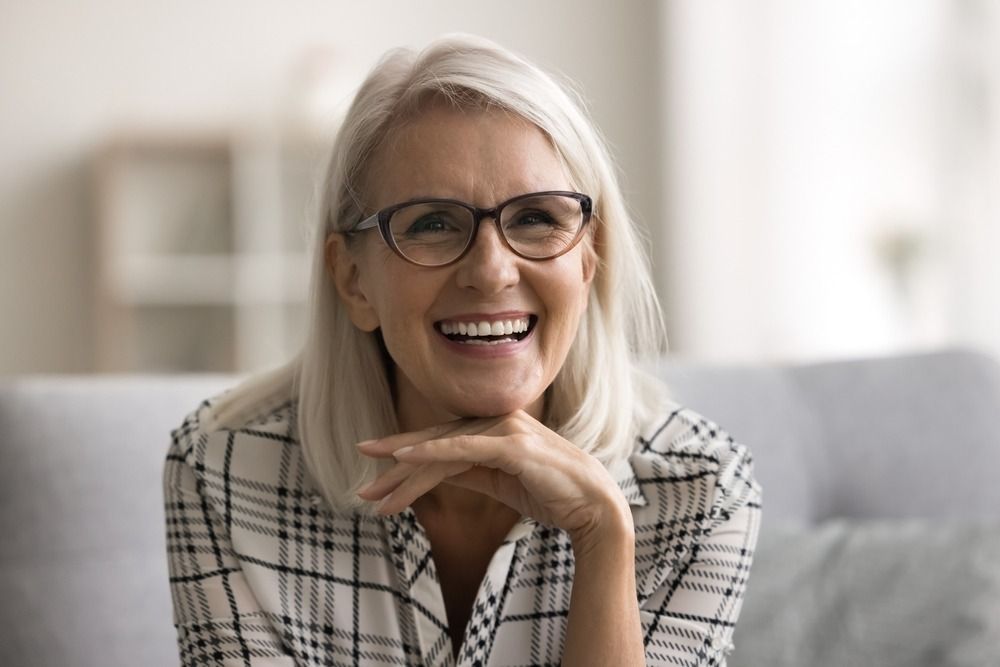 Smiling woman with glasses resting her chin on her hand on a light-colored sofa