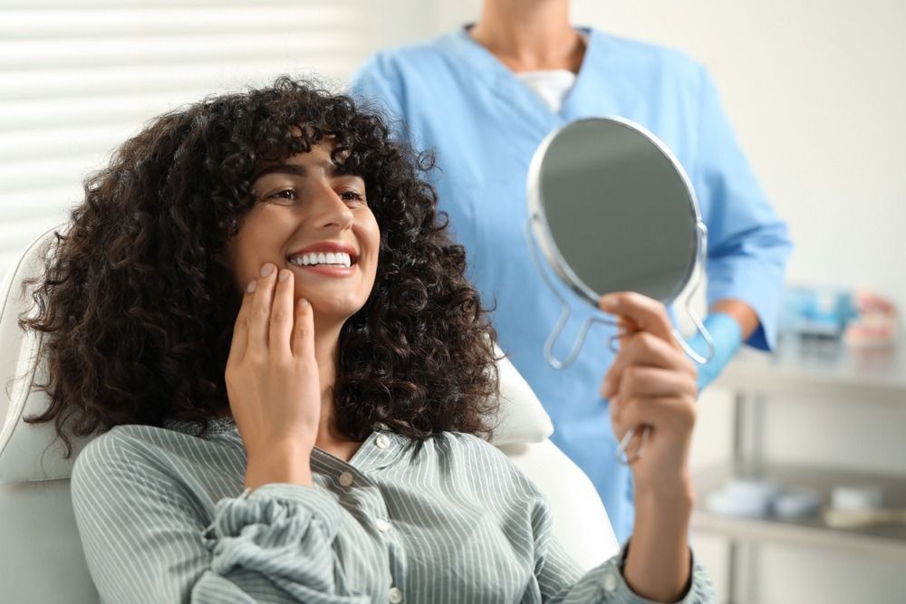 Smiling person holding a mirror and touching their cheek in a dental exam room