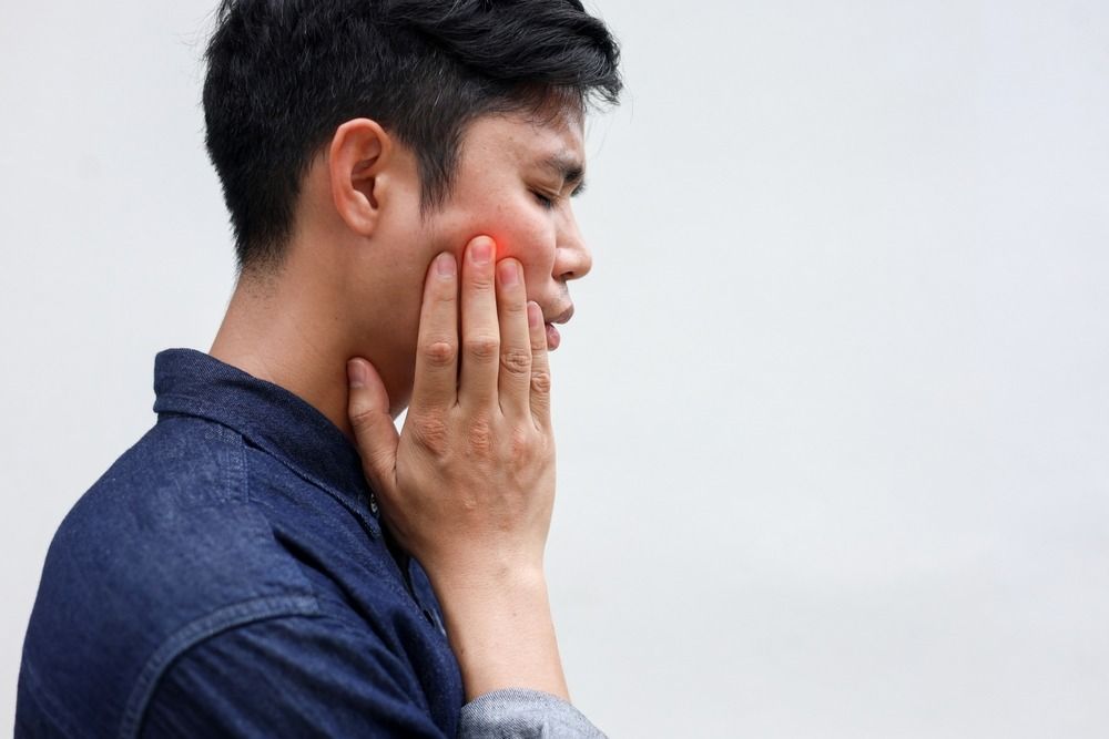 Person in profile touching a red cheek, appearing to have jaw or tooth pain against a plain background
