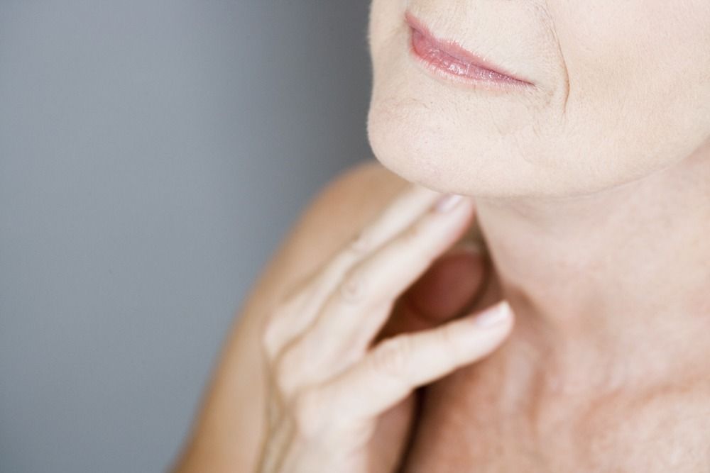 Close-up of a hand touching the side of a person’s neck and chin against a gray background