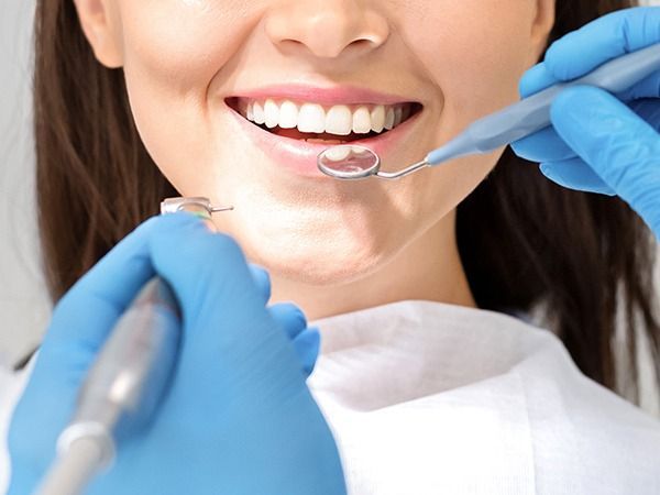 Dentist using tools to examine a smiling patient’s teeth in a clinic