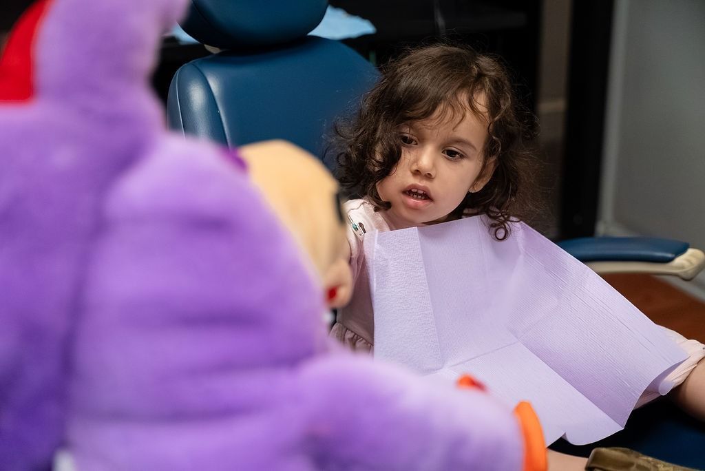 Child in a purple bib looking at someone in a purple outfit at a table