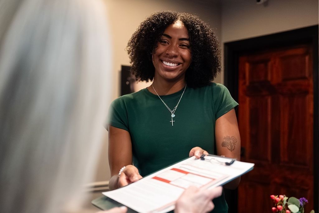 Smiling woman in a green shirt handing over a clipboard at a reception desk