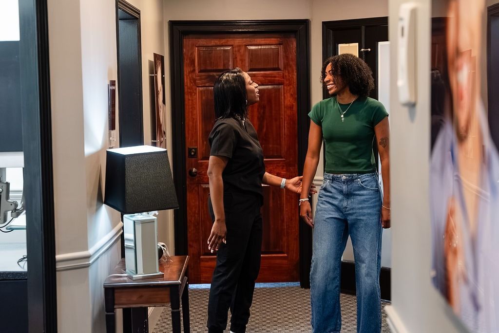 Two people talking in a hallway, one holding the other's hand near a wooden door.