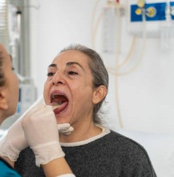 Dentist examining a patient's open mouth with gloved hands in a clinic.