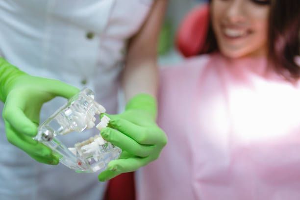 Dentist in green gloves holding a clear dental aligner.