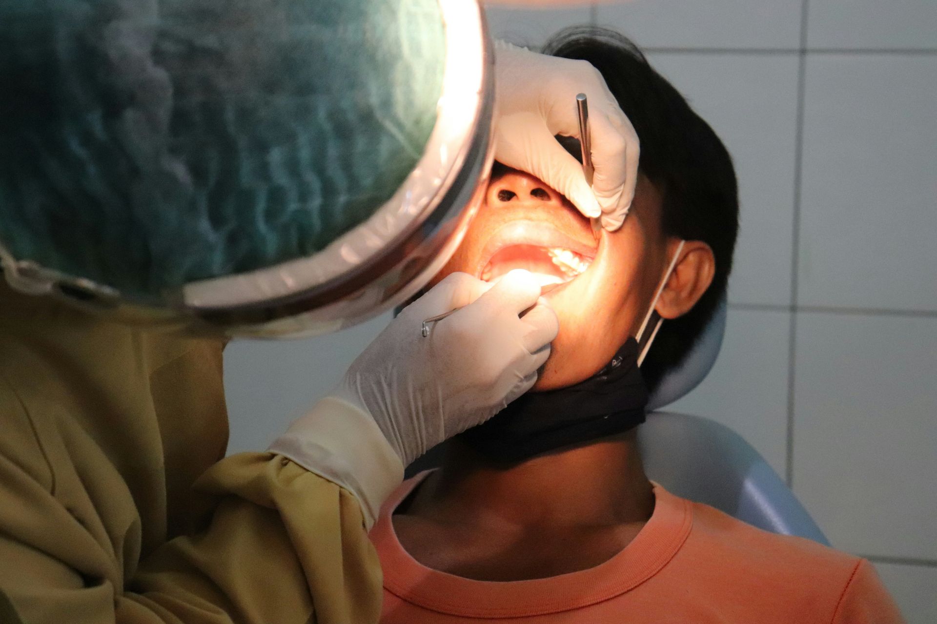 Dentist examining a patient’s mouth with a bright dental light and gloved hands.