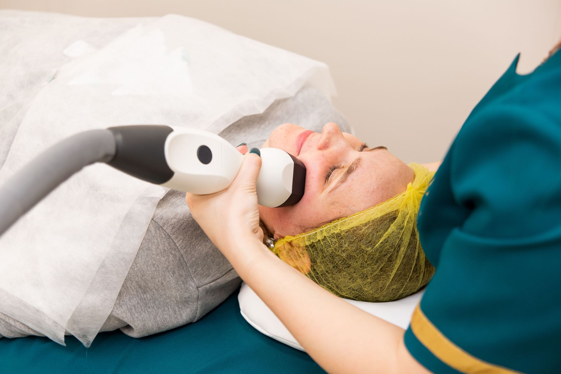 Person receiving facial treatment with a handheld device while lying on a spa bed.