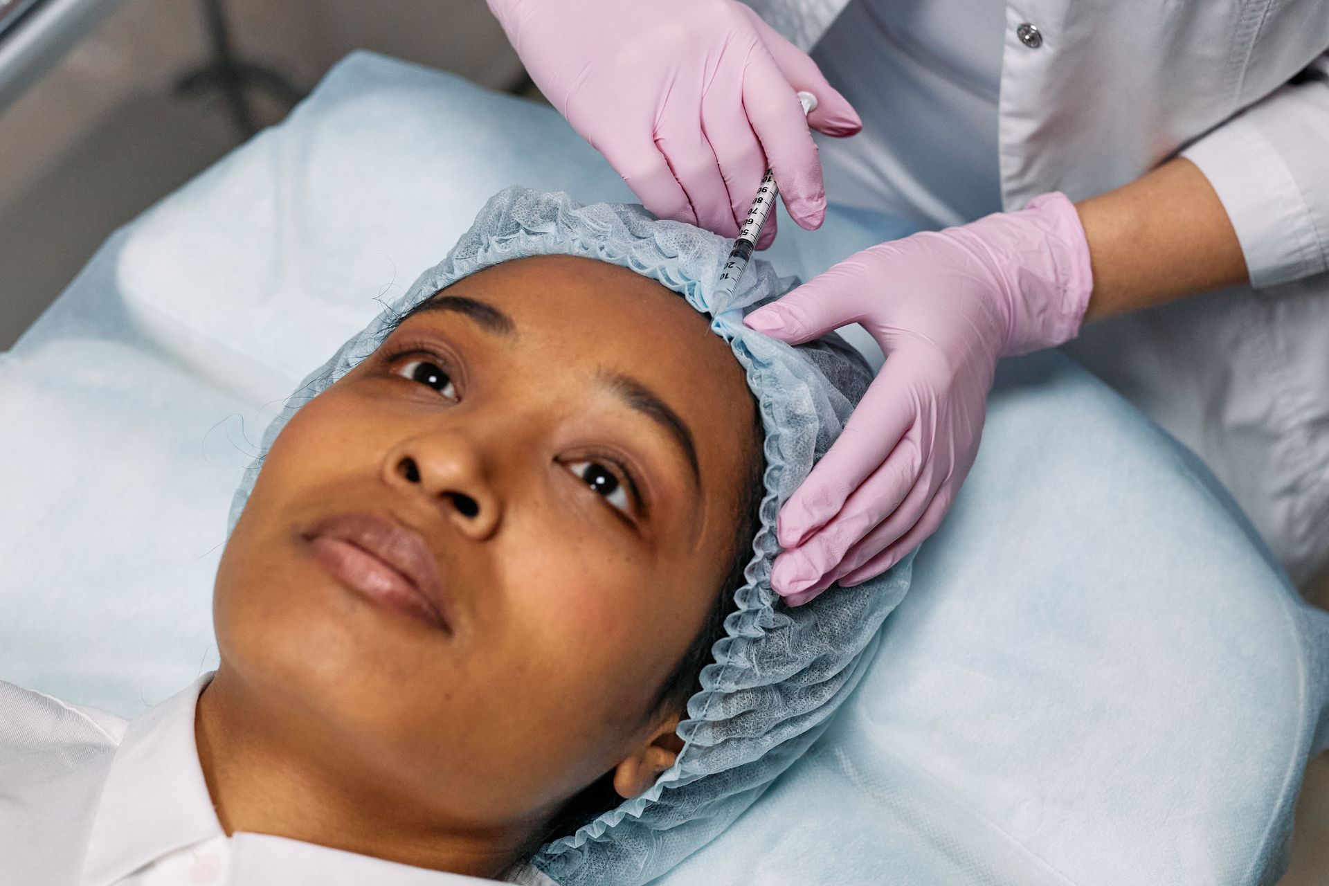 Patient lying on a treatment bed while gloved hands adjust a disposable head covering.