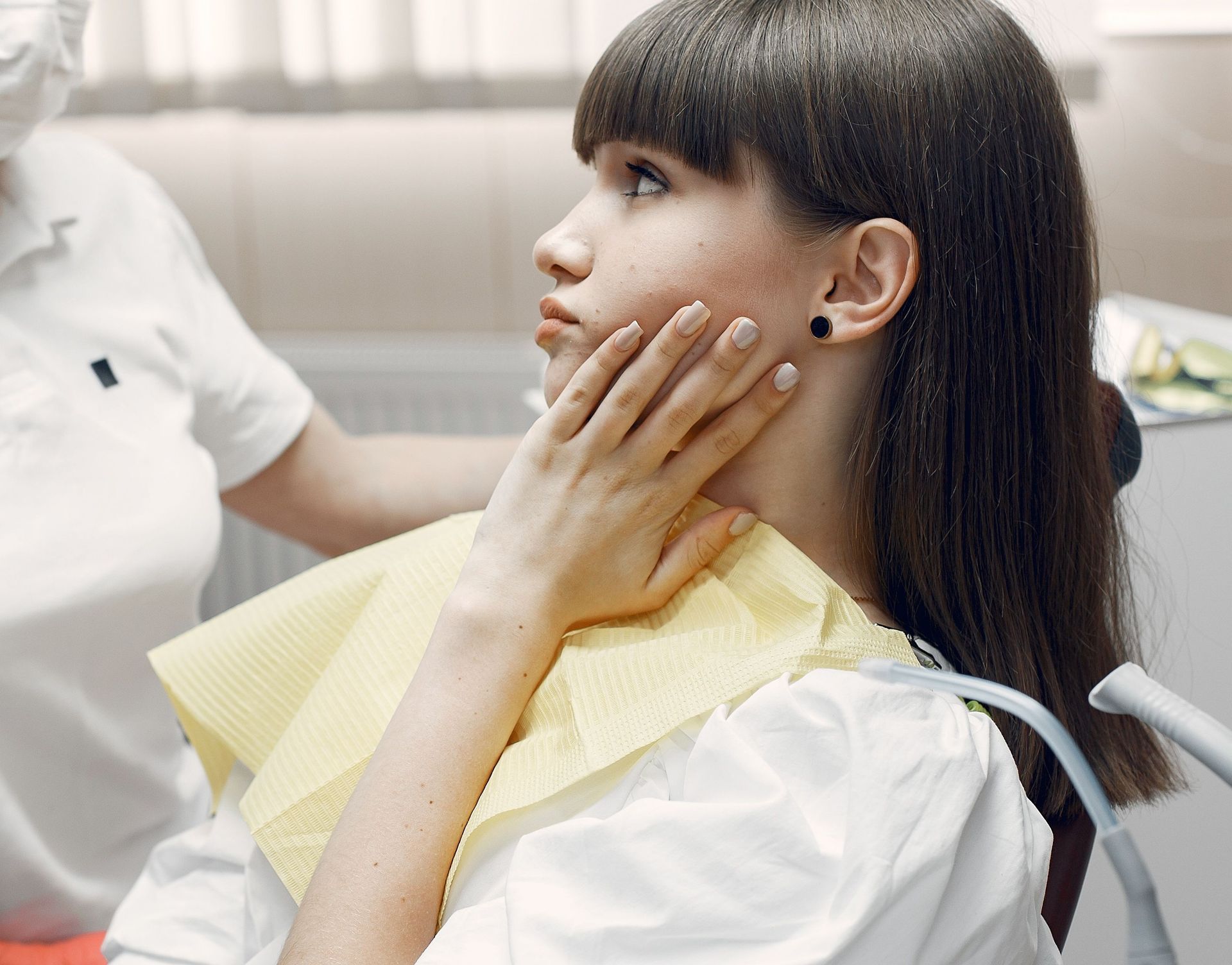 Woman in a dental chair touching her cheek while a dentist stands beside her.