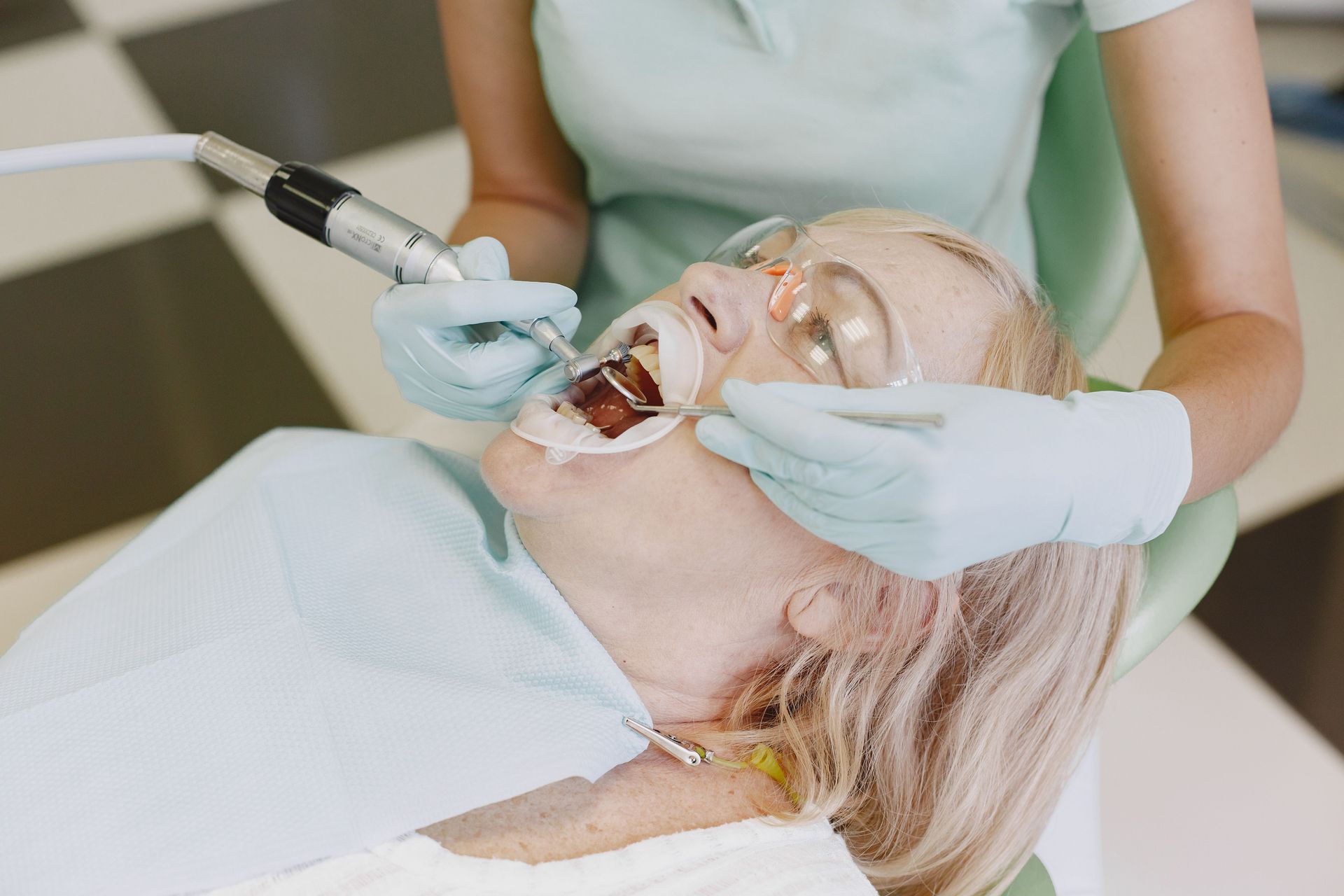 Dental hygienist cleaning a patient’s teeth with suction and mirror in a clinic.