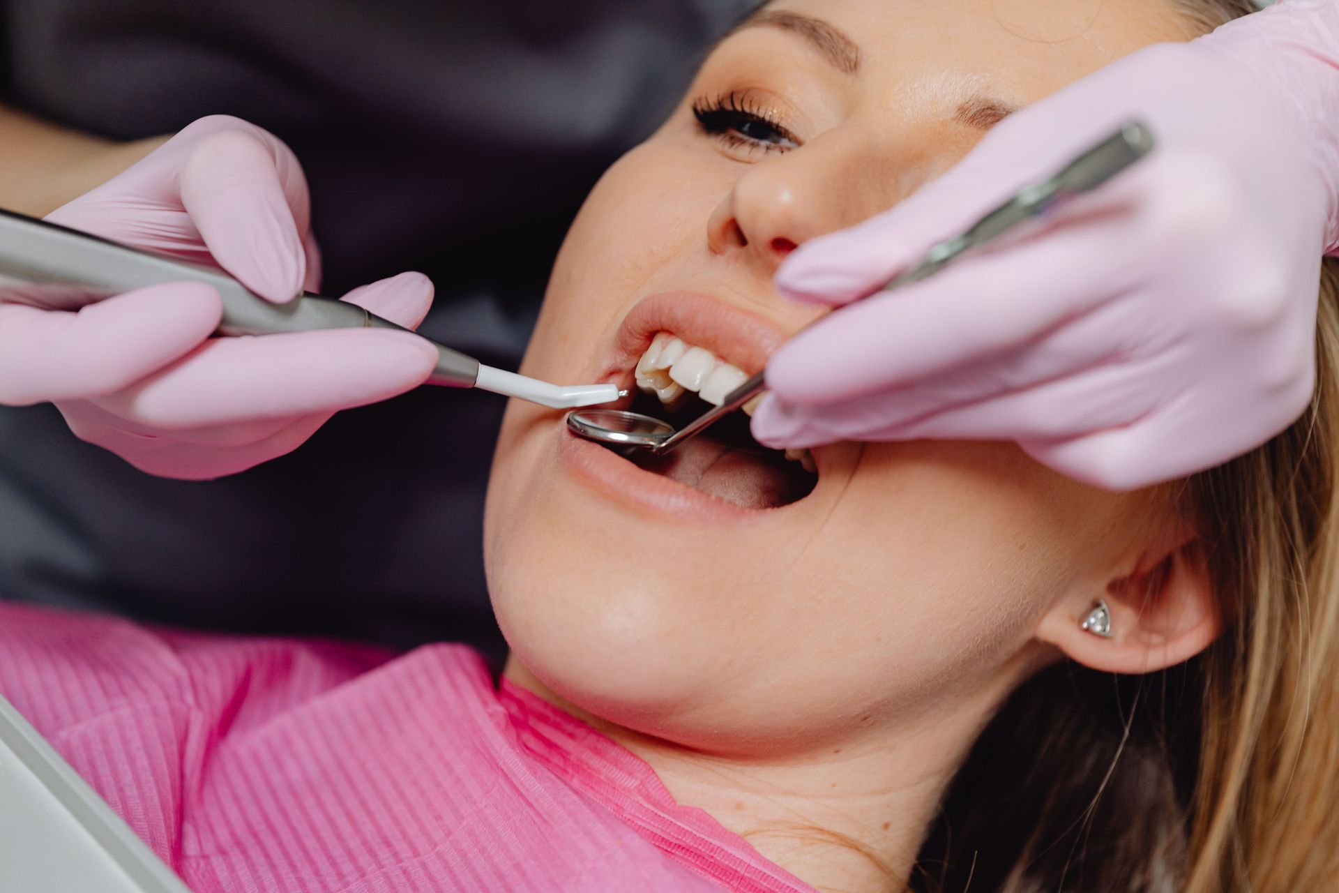 Dentist examining a patient’s teeth with tools and pink gloves in a dental chair.