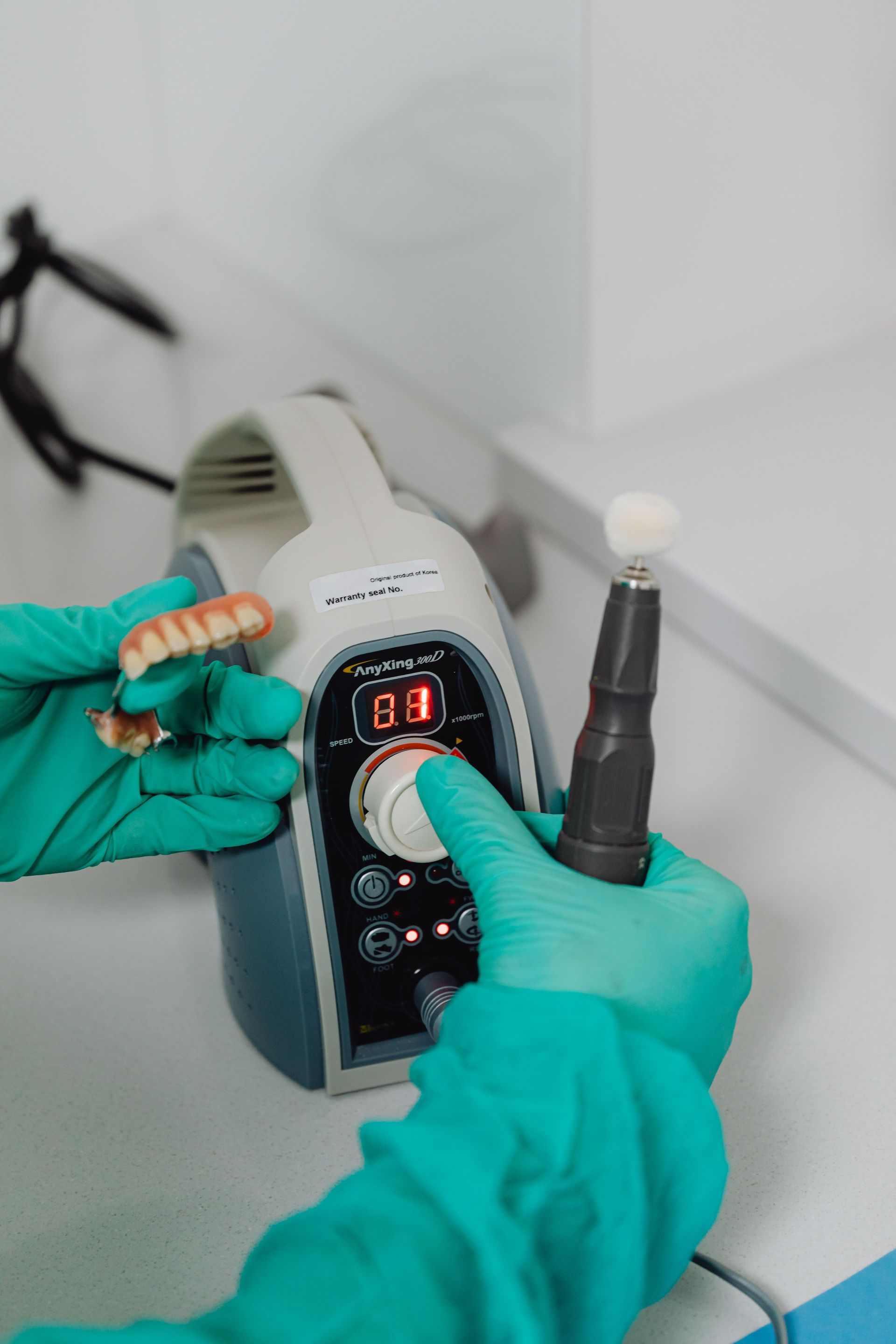 Gloved hands use a handheld device with a digital display and brush tip on a countertop..