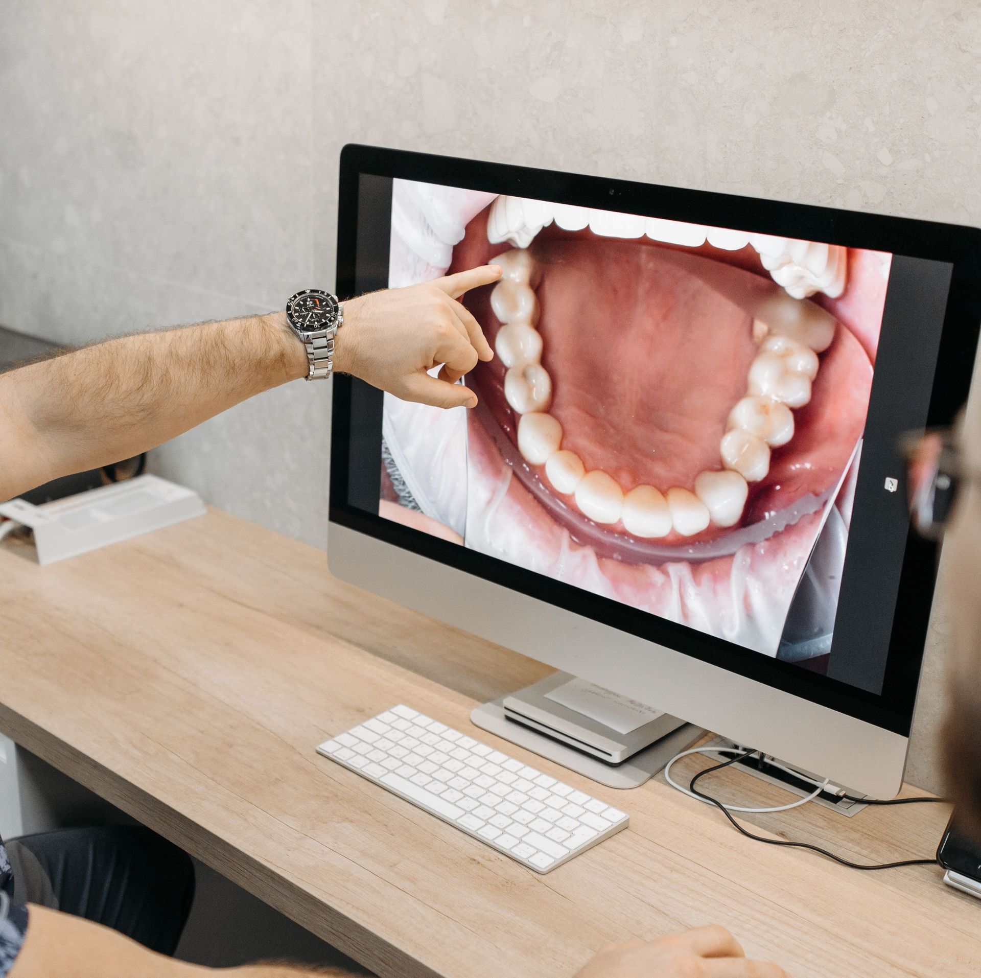 Dentist pointing at a close-up teeth scan on a desktop monitor in a clean office.