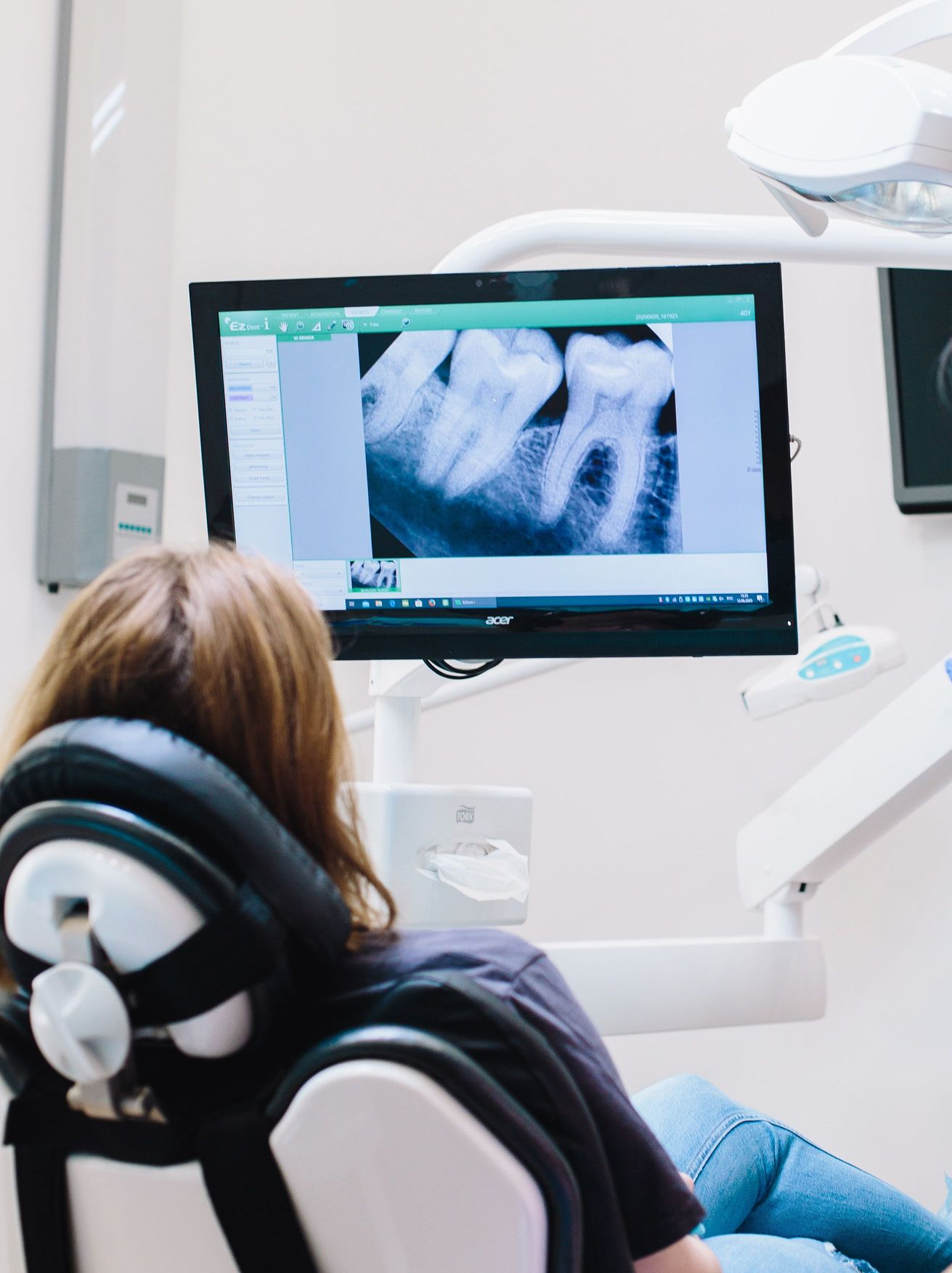 Dentist chair facing a monitor showing X-ray images in a bright dental clinic.