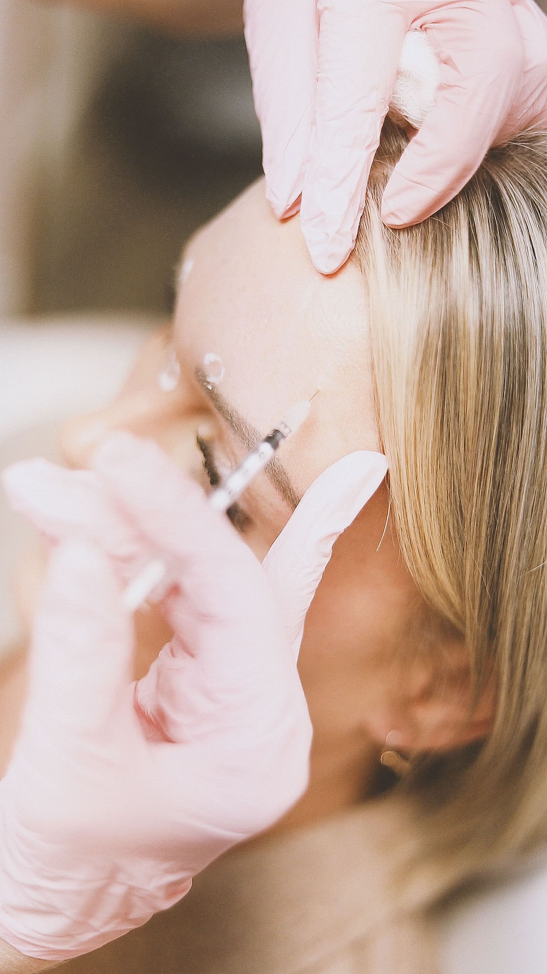 Gloved hands applying makeup to a woman's face with a brush during a beauty treatment.