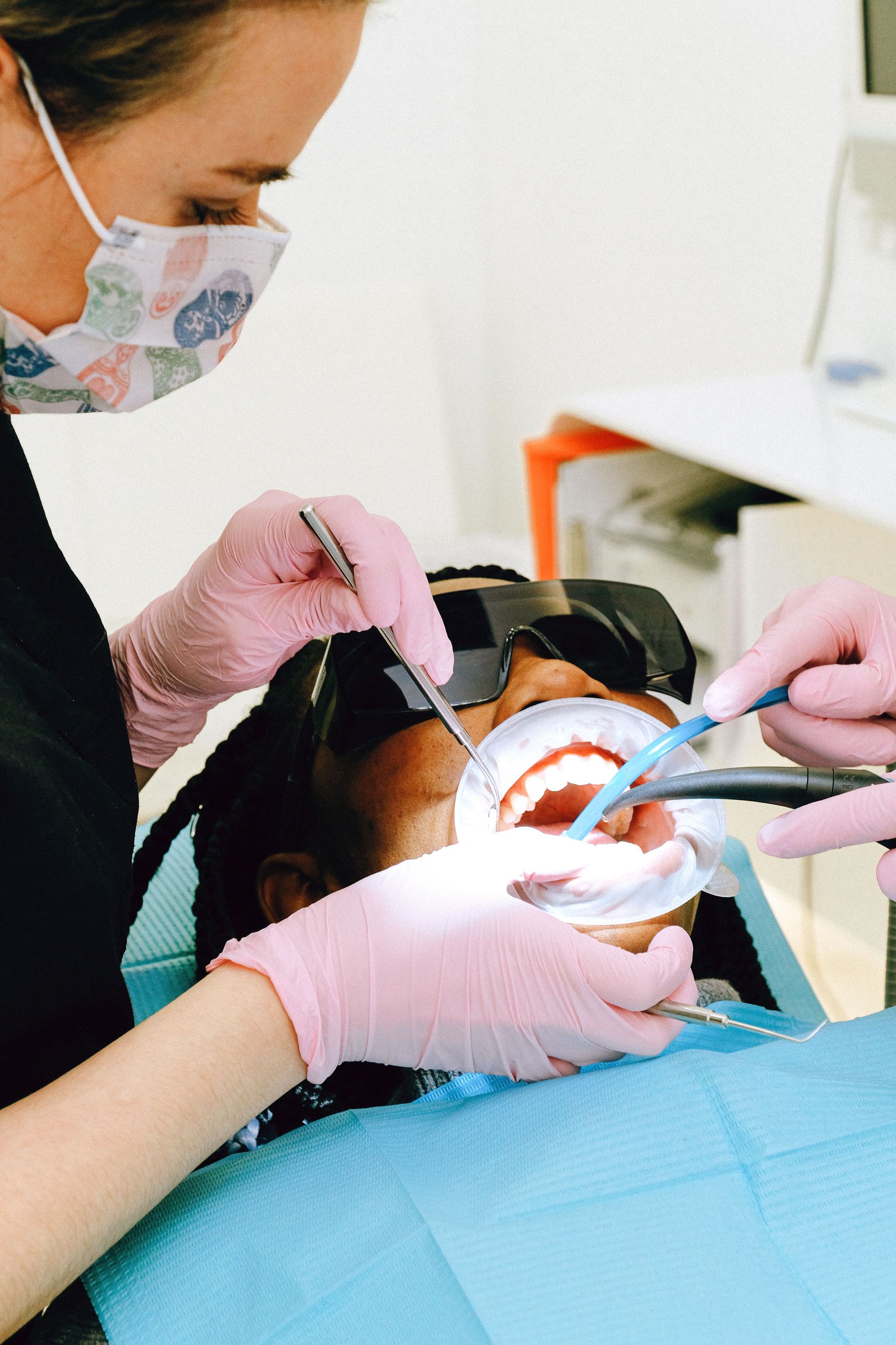 Dentist treating a patient’s open mouth with tools and suction, wearing gloves and a mask.