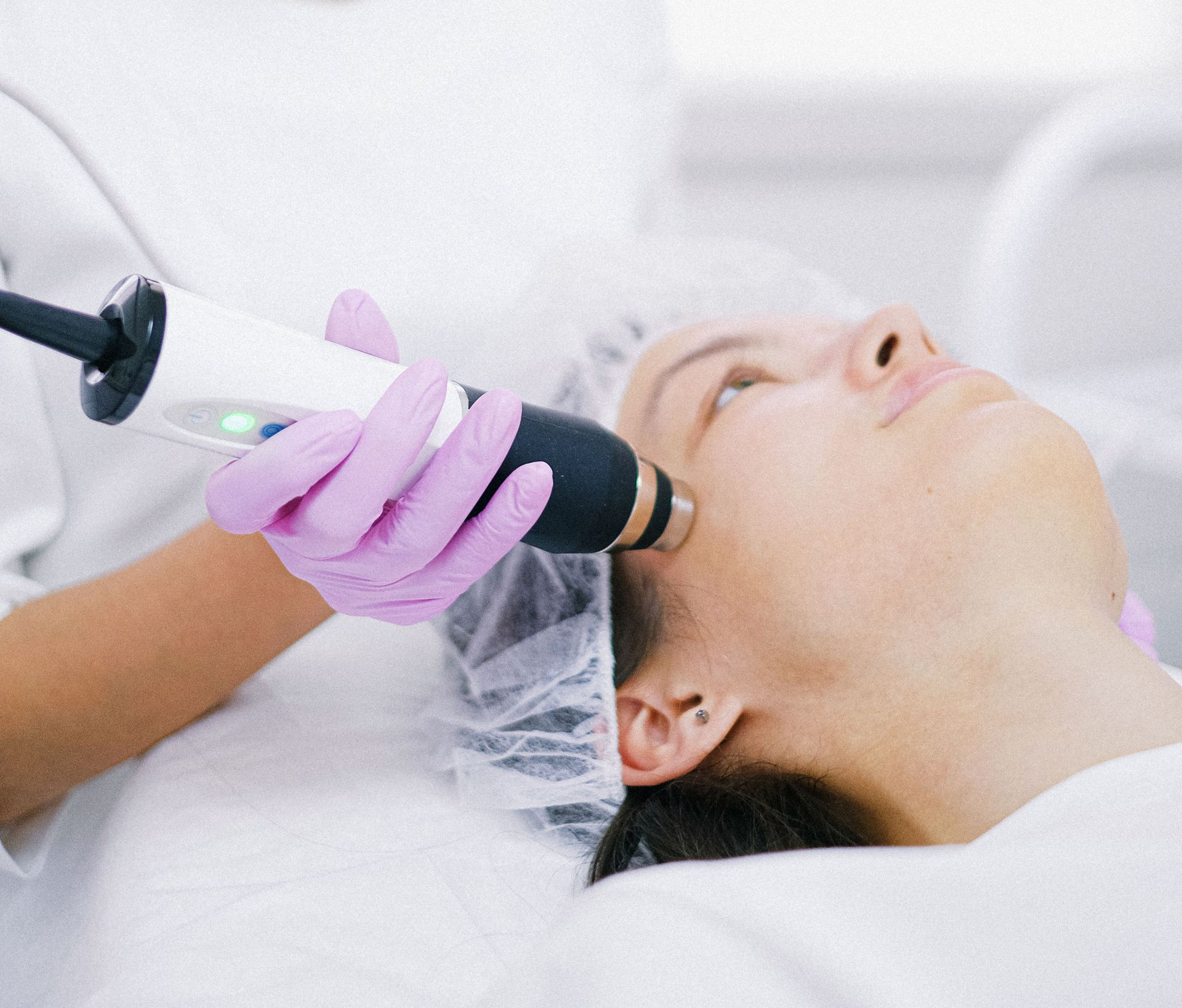 Gloved clinician using a handheld device on a patient’s face in a spa treatment setting.