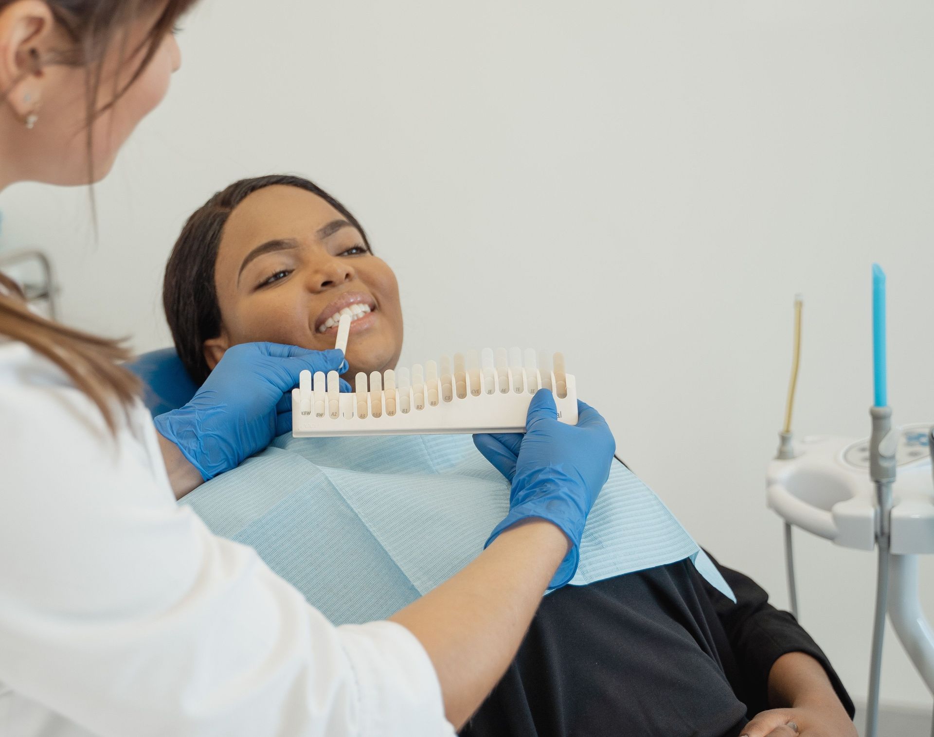 Dentist in blue gloves examines a smiling patient in a dental chair.
