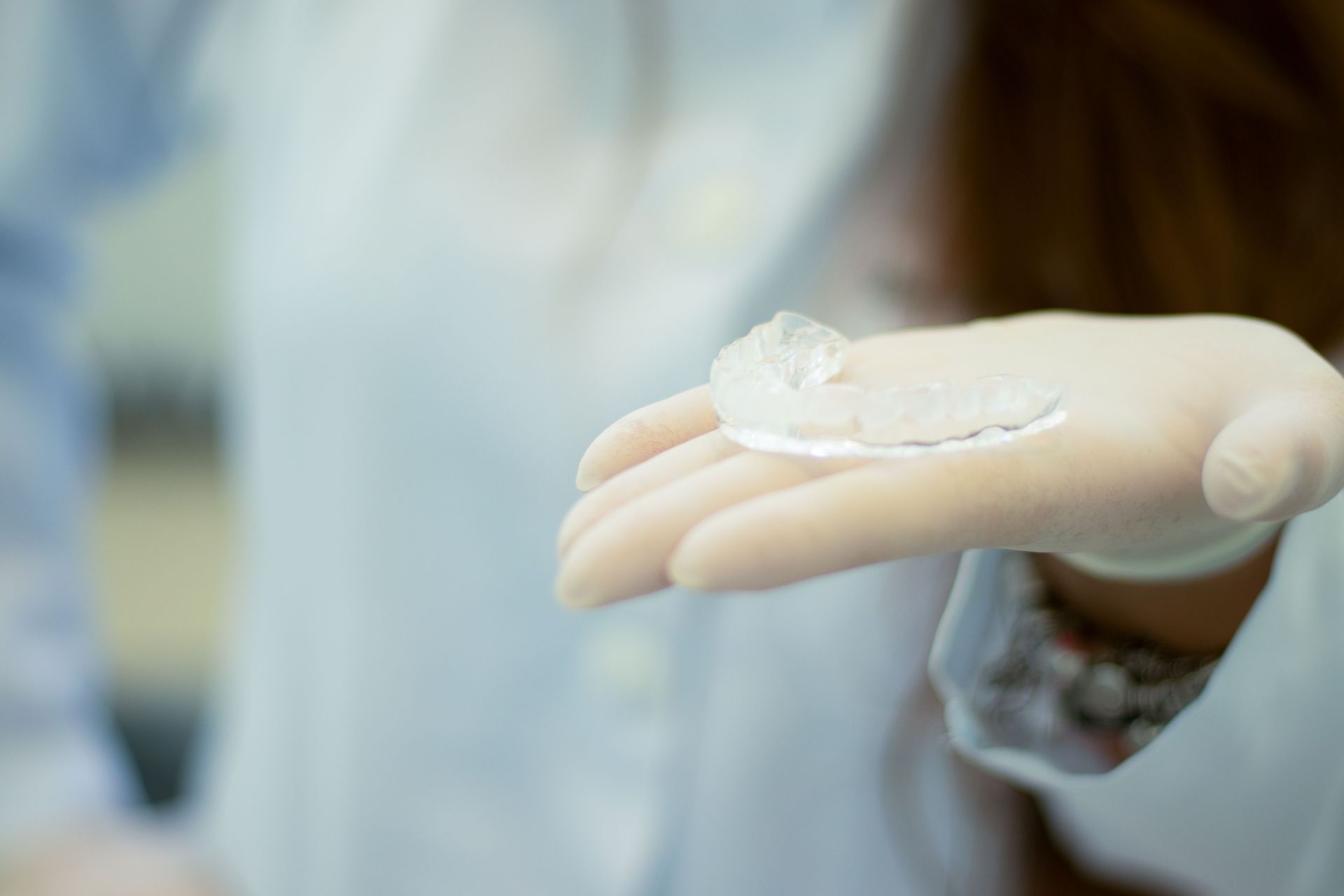 Gloved hand holding a clear contact lens in a clinical setting.