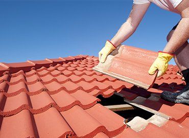 Person replacing a red roof tile on a sunny day.