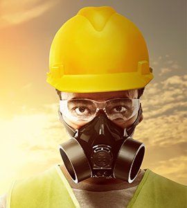 Person wearing yellow hard hat, safety glasses, and respirator in a sunny outdoor setting.