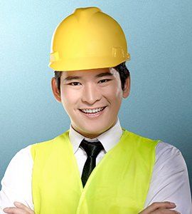 Man wearing yellow hard hat and vest smiles, arms crossed.