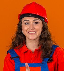 Woman wearing red hard hat and jumpsuit gives thumbs up, smiling.