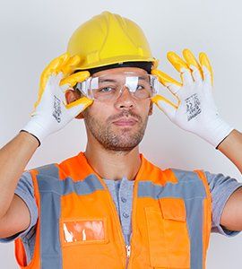 Construction worker wearing safety gear, adjusting eyeglasses, in a bright environment.