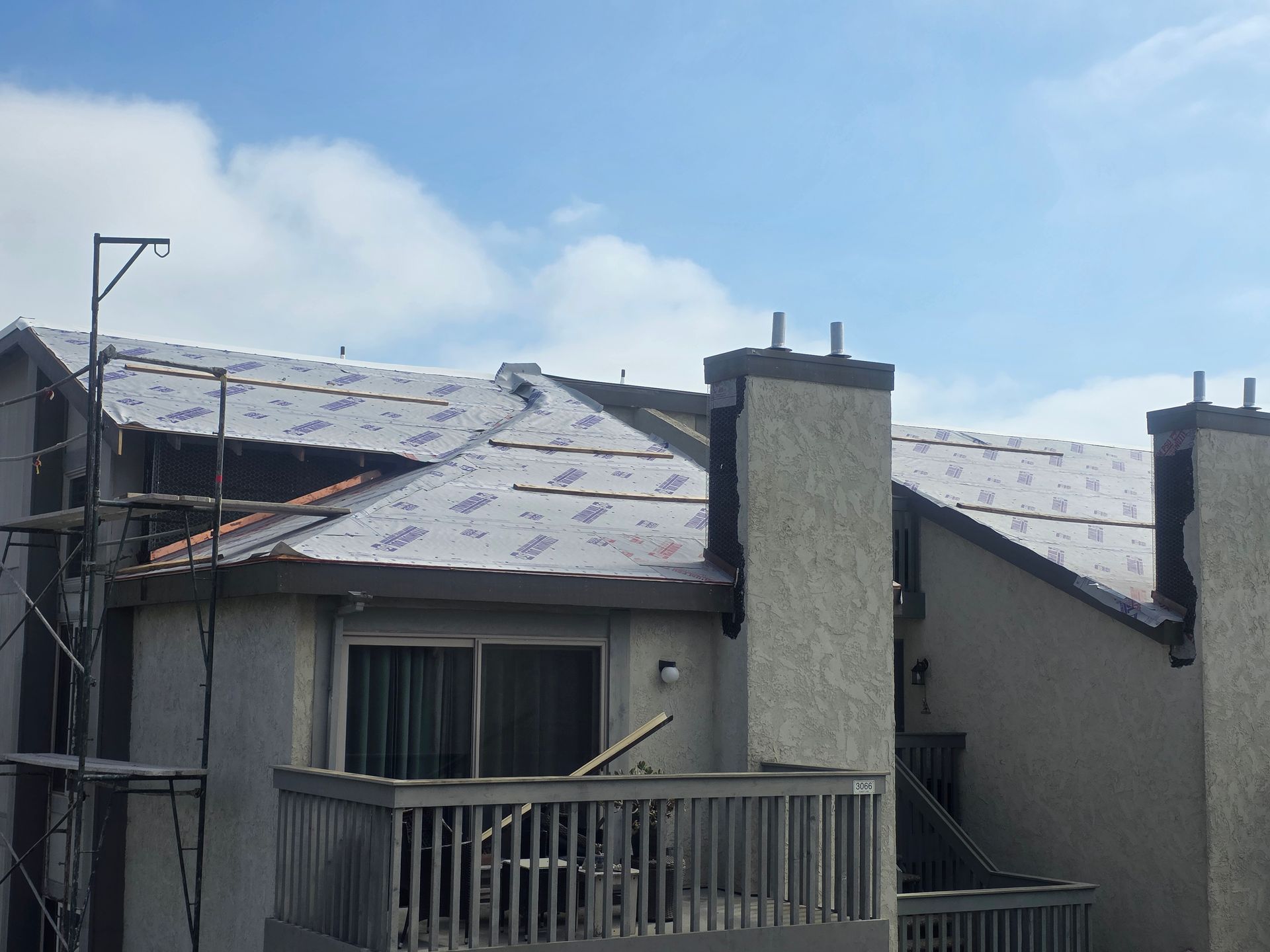 Apartment roof under construction, covered with underlayment; scaffolding on side, sunny day.