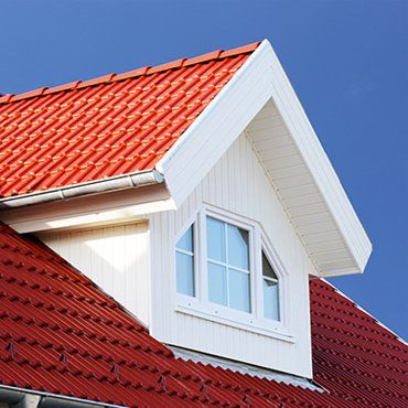 Red tile roof with white dormer and window against a blue sky.