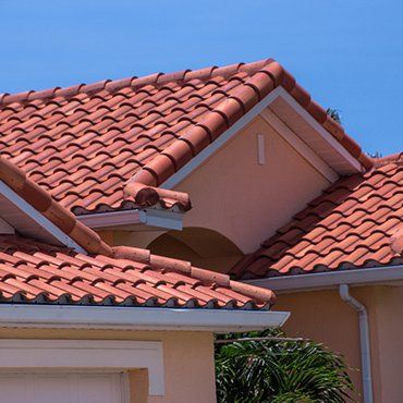 Red clay tile roof on a pale peach house with a clear blue sky background.