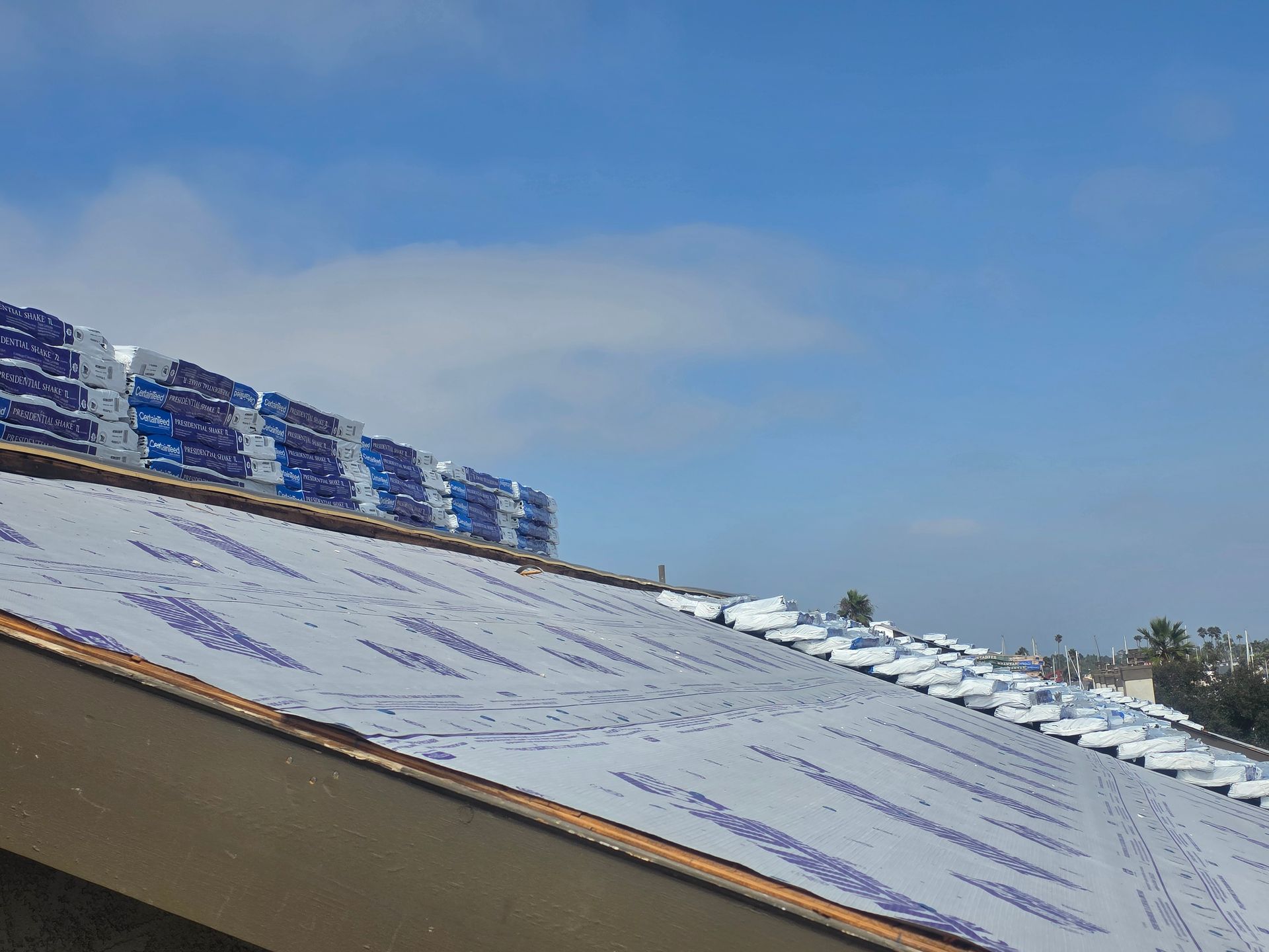 Roof with stacked bundles of blue material, blue sky in background.