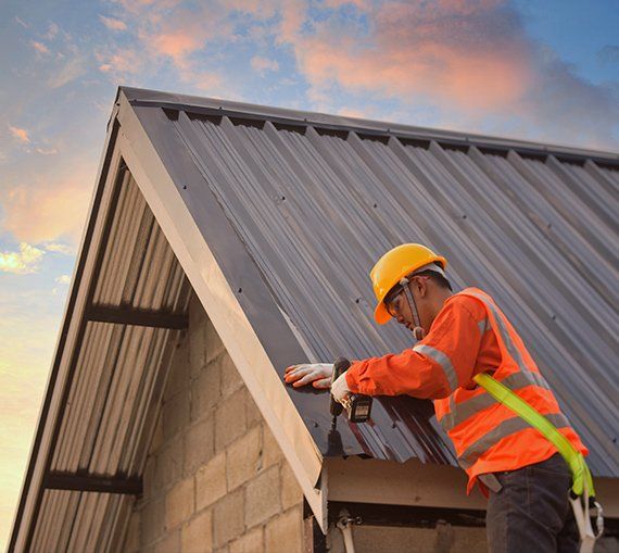Roofer in safety gear installing metal panels on a building roof. Bright yellow vest, helmet, blue sky.