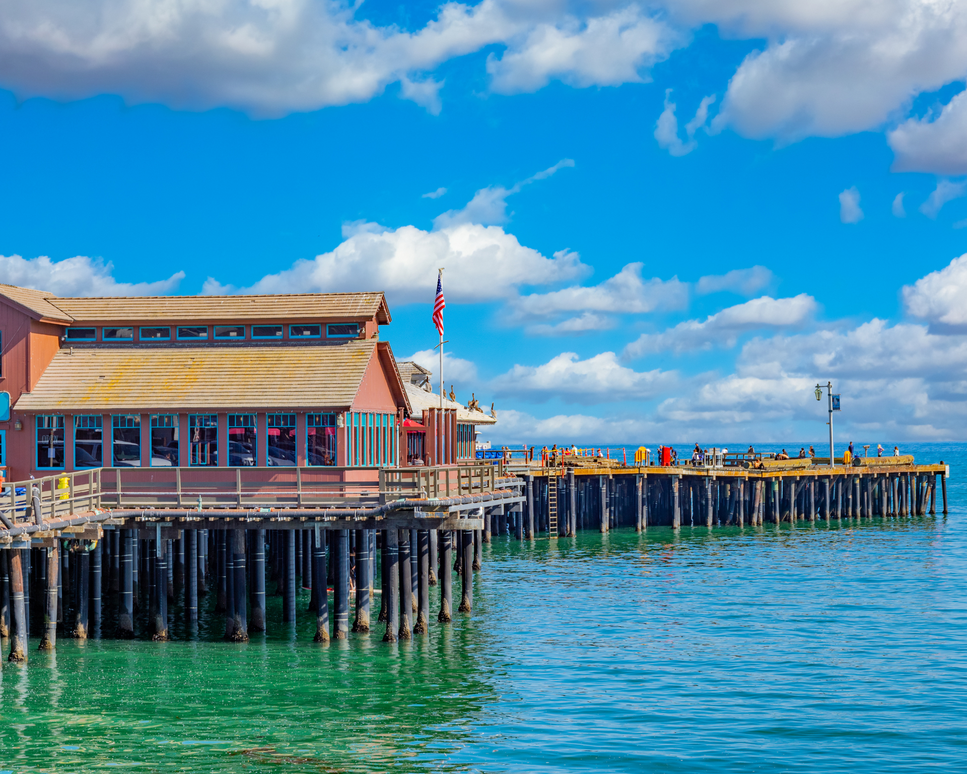 Wooden pier with building over turquoise water under a blue sky with fluffy clouds.