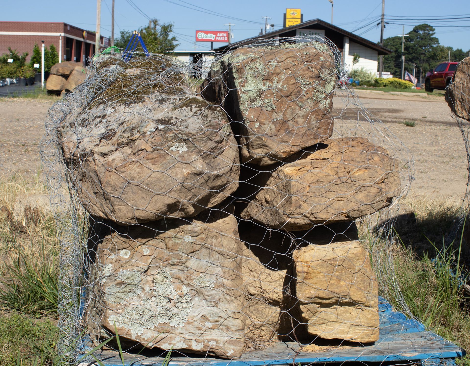 Stacked large rough boulders on a blue pallet outdoors beside a road