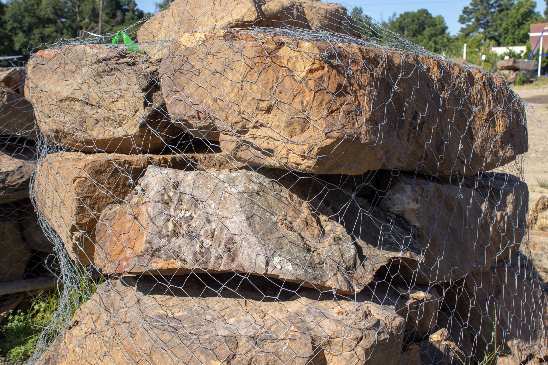Stacked large rocks covered with wire mesh outdoors in sunlight