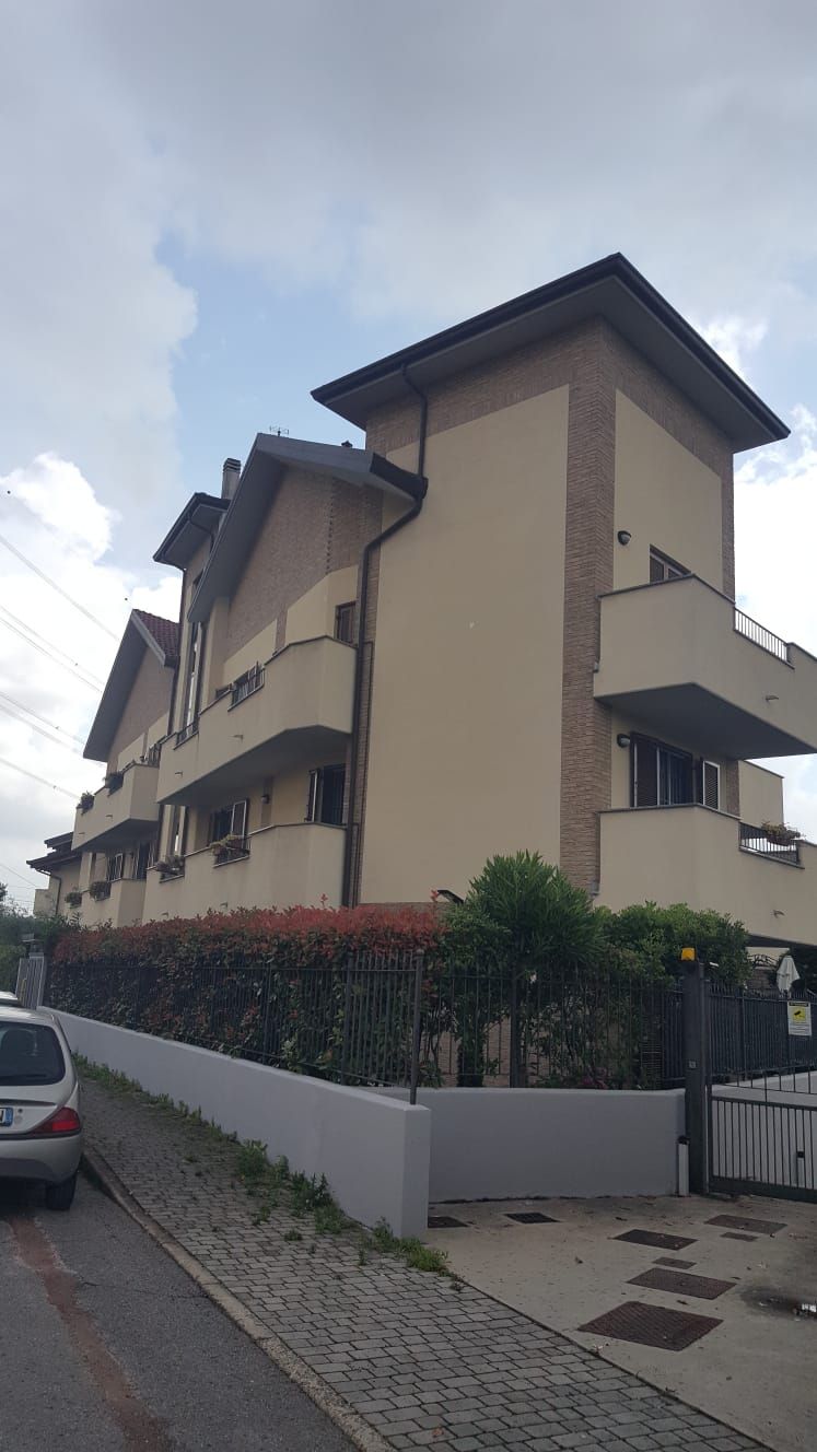 Edificio a più piani con balconi, esterno beige chiaro, dettagli in mattoni e una siepe verde lungo un muretto.