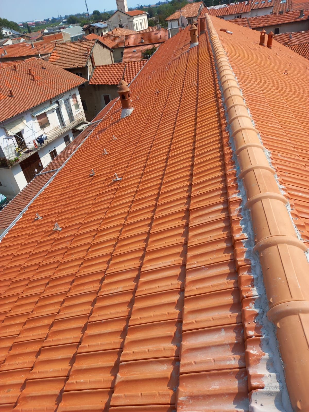 Tetti di tegole rosse degli edifici di una città, con comignoli e un cielo soleggiato.