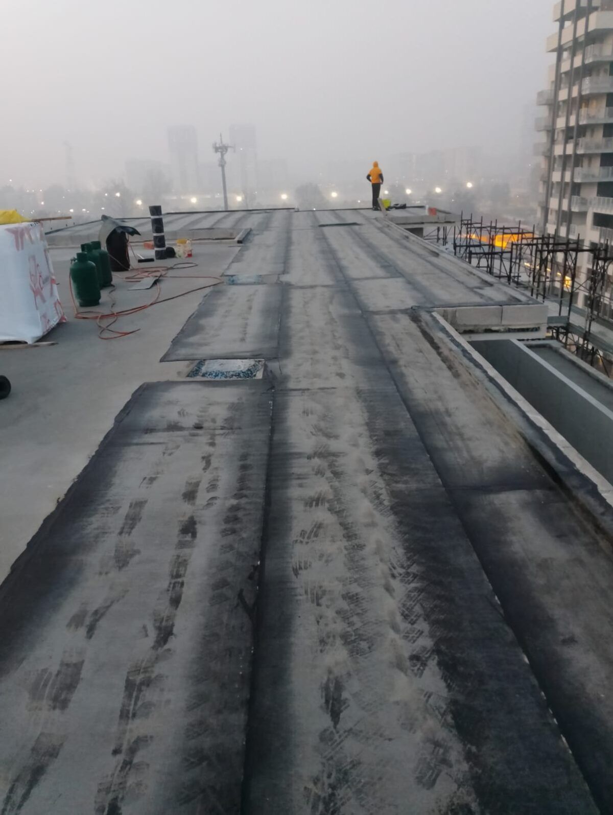 Cantiere edile sul tetto in una giornata nebbiosa con un operaio che indossa un gilet arancione.