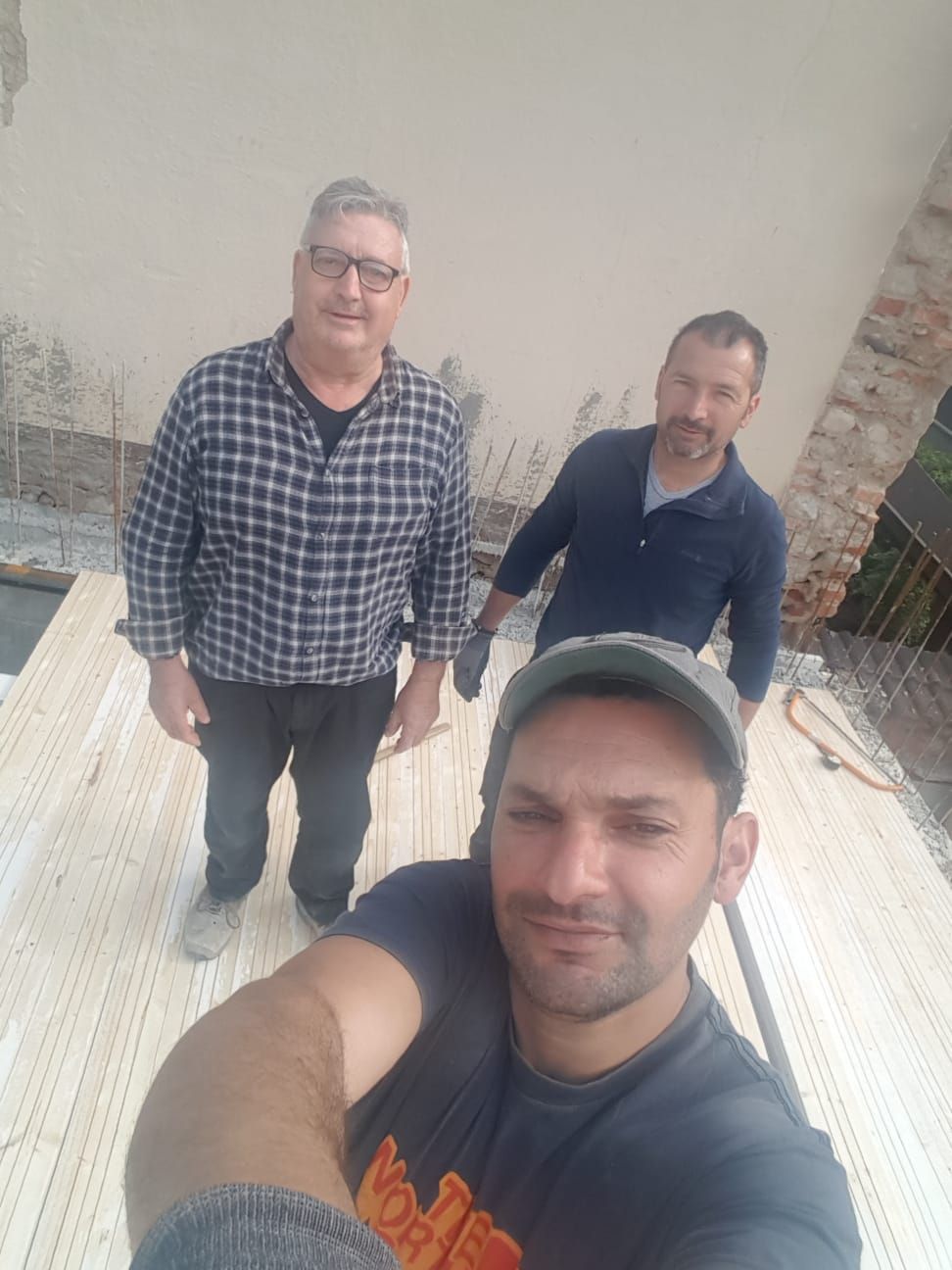 Tre operai edili posano su una superficie di legno; uno si scatta un selfie.